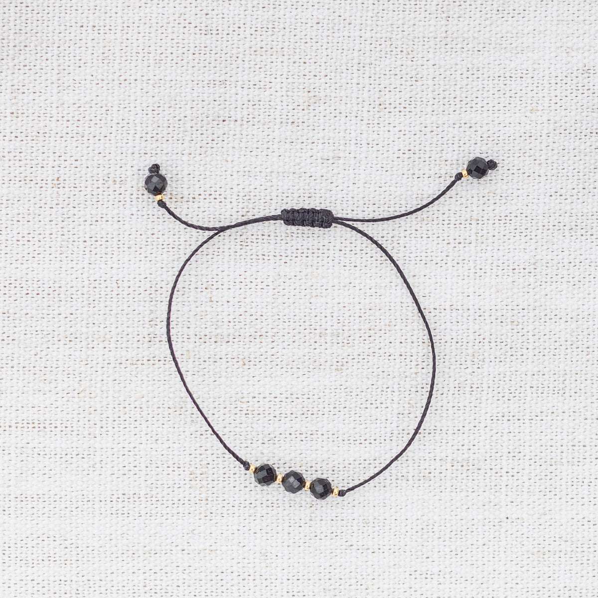 Intuitive Charms Ceto's Mist Black tourmaline Braided natural Crystal beaded custom Bracelet in gold and black cord on a light fabric background