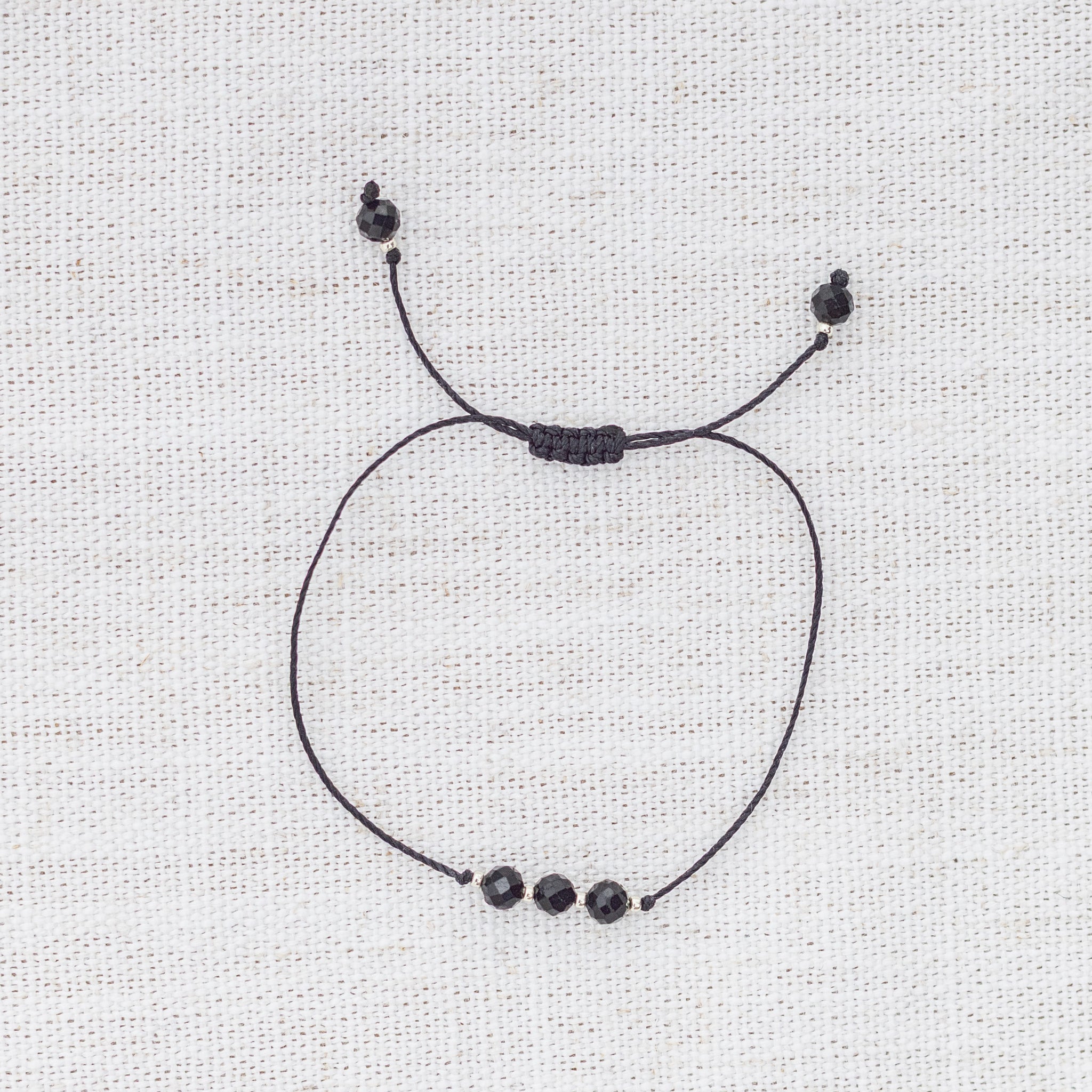 Intuitive Charms Ceto's Mist Black tourmaline Braided natural Crystal beaded custom Bracelet in silver and black cord on a light fabric background