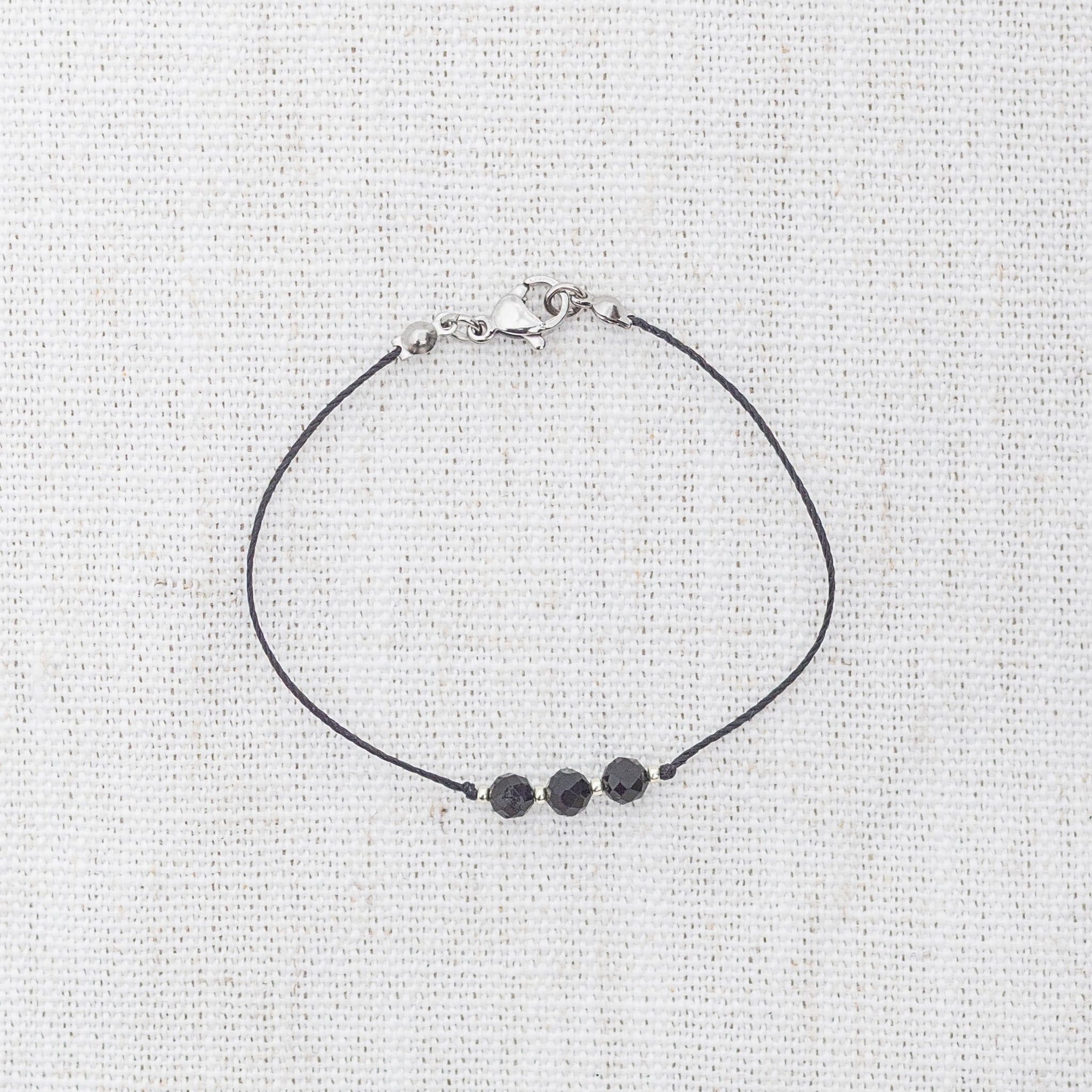 Intuitive Charms Ceto's Mist Black tourmaline Braided natural Crystal beaded custom Bracelet in silver and black cord and clasp on a light fabric background