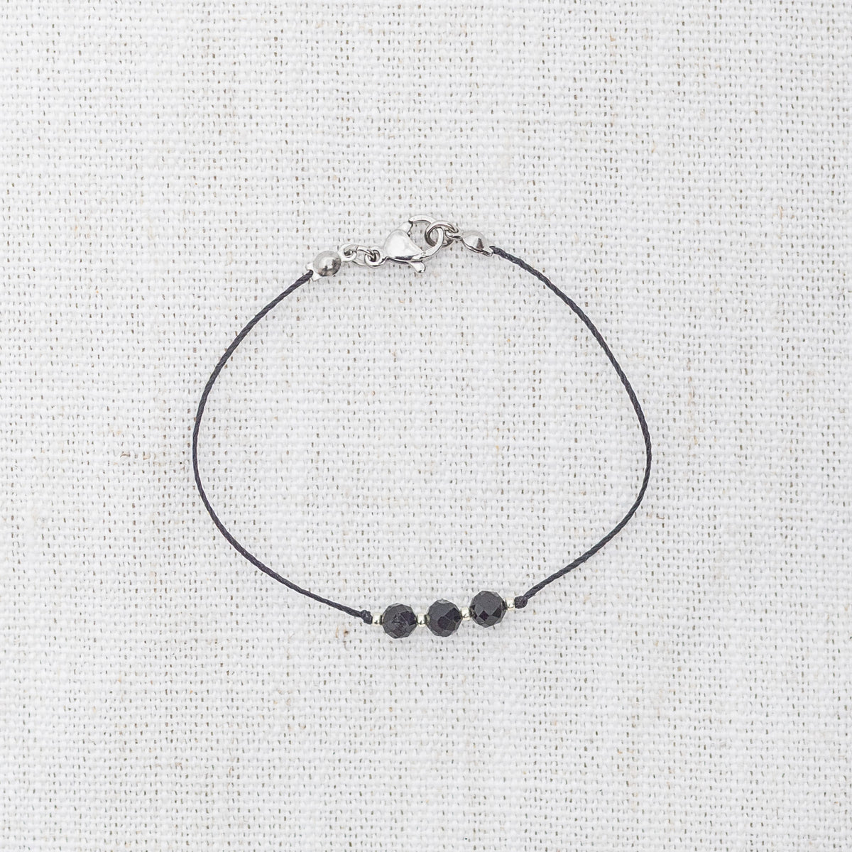 Intuitive Charms Ceto's Mist Black tourmaline Braided natural Crystal beaded custom Bracelet in silver and black cord and clasp on a light fabric background