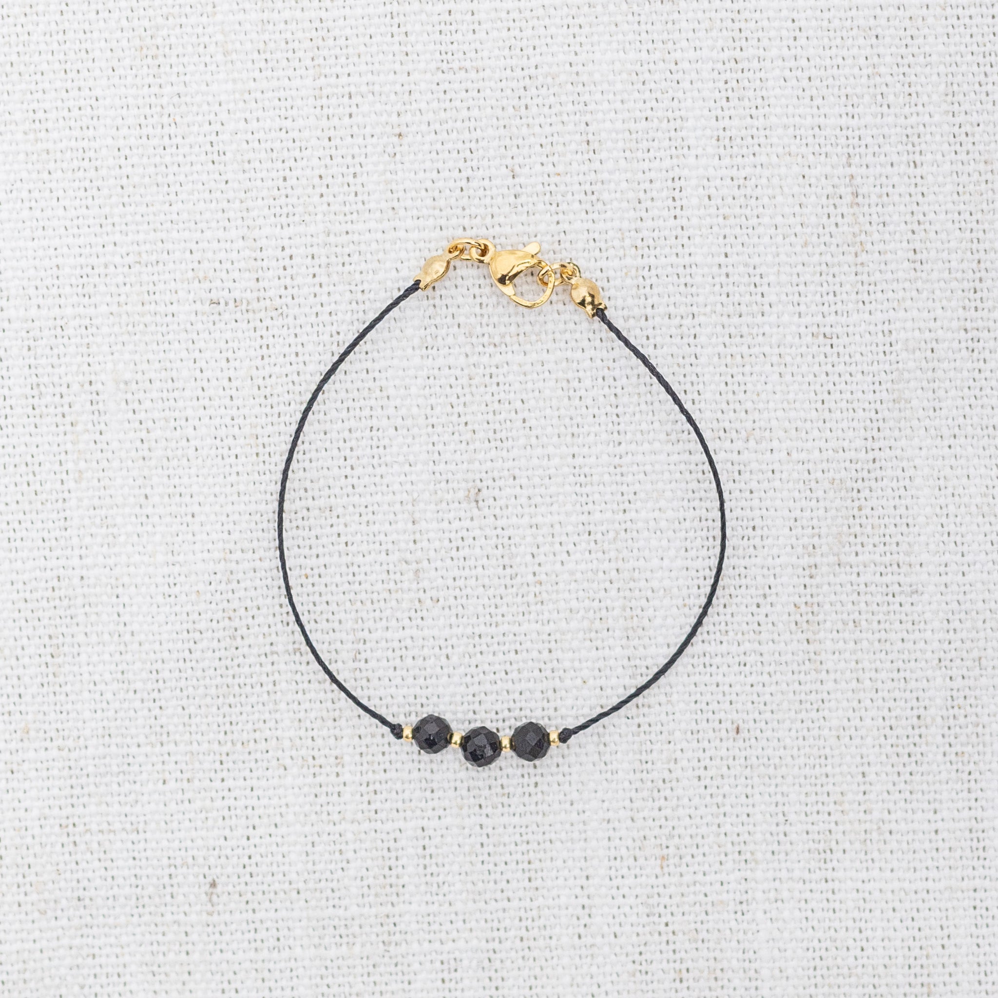 Intuitive Charms Ceto's Mist Black tourmaline Braided natural Crystal beaded custom Bracelet in gold and black cord and clasp on a light fabric background